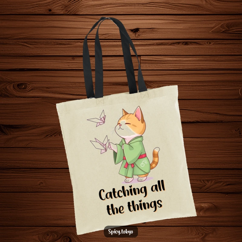 Funny cat in a green kimono playfully attempting to catch a floating origami crane on a tote bag.